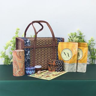 Woven rattan tote basket with leather handles, set out with batik wrapped items, two yellow snack pouches and a printed card.