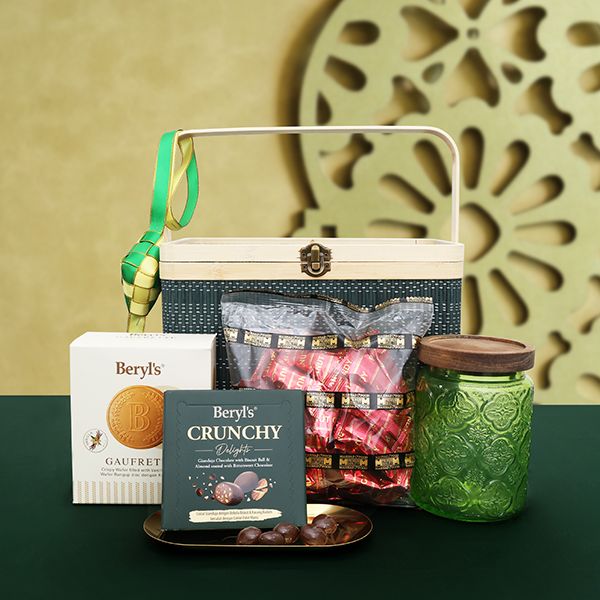 Open hamper box with a wooden lid holding a glass canister of pink sweets, a boxed cookie tin, a snack pouch and a honey jar.