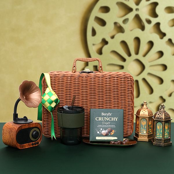Rattan hamper case opened to show a wooden speaker, a thermos flask, a cookie box and brass lanterns, dressed with a woven ketupat.