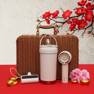 Rattan hamper standing behind a dusty pink thermos tumbler and a round pink speaker, on red with gold ingots and pink blooms.