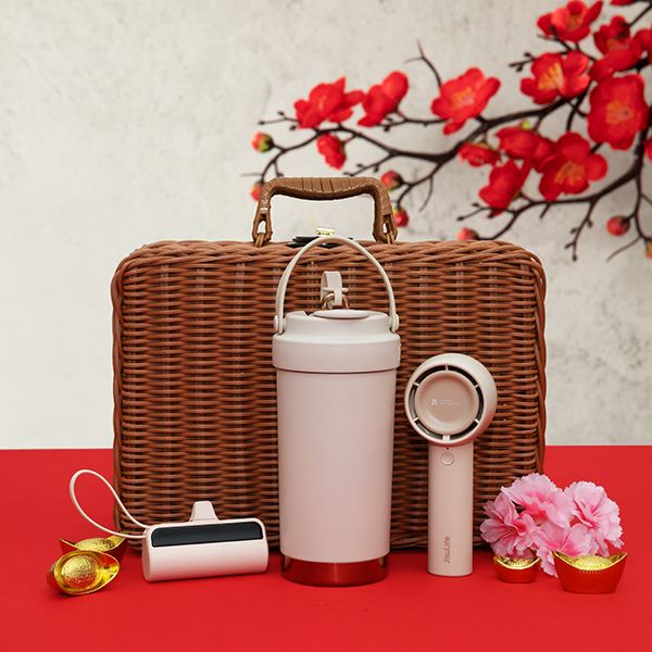 Rattan hamper standing behind a dusty pink thermos tumbler and a round pink speaker, on red with gold ingots and pink blooms.