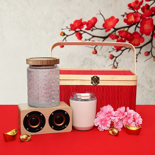 Red tasselled hamper box with a glass canister of pink sweets, a pink tumbler and a wooden twin driver speaker on gold ingots.