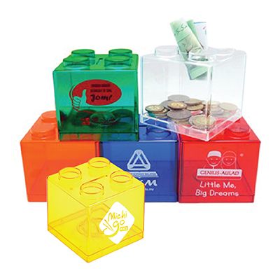 Translucent brick-shaped coin boxes stacked in green, clear, orange, blue, red and yellow, holding coins and notes, with printed artwork.