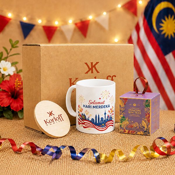 Kraft gift box printed with a logo, a white mug reading Selamat Hari Merdeka, a round wooden coaster and a patterned carton.