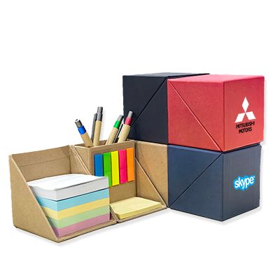 Kraft paper cube memo holder opened flat with a note pad, coloured sticky tabs and pens, shown beside closed cubes in red, blue and dark grey printed with a logo.