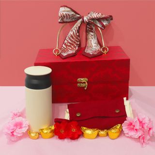 Red wooden hamper box tied with ribbon bows, standing with a cream thermos and a red packet holder among gold ingots.
