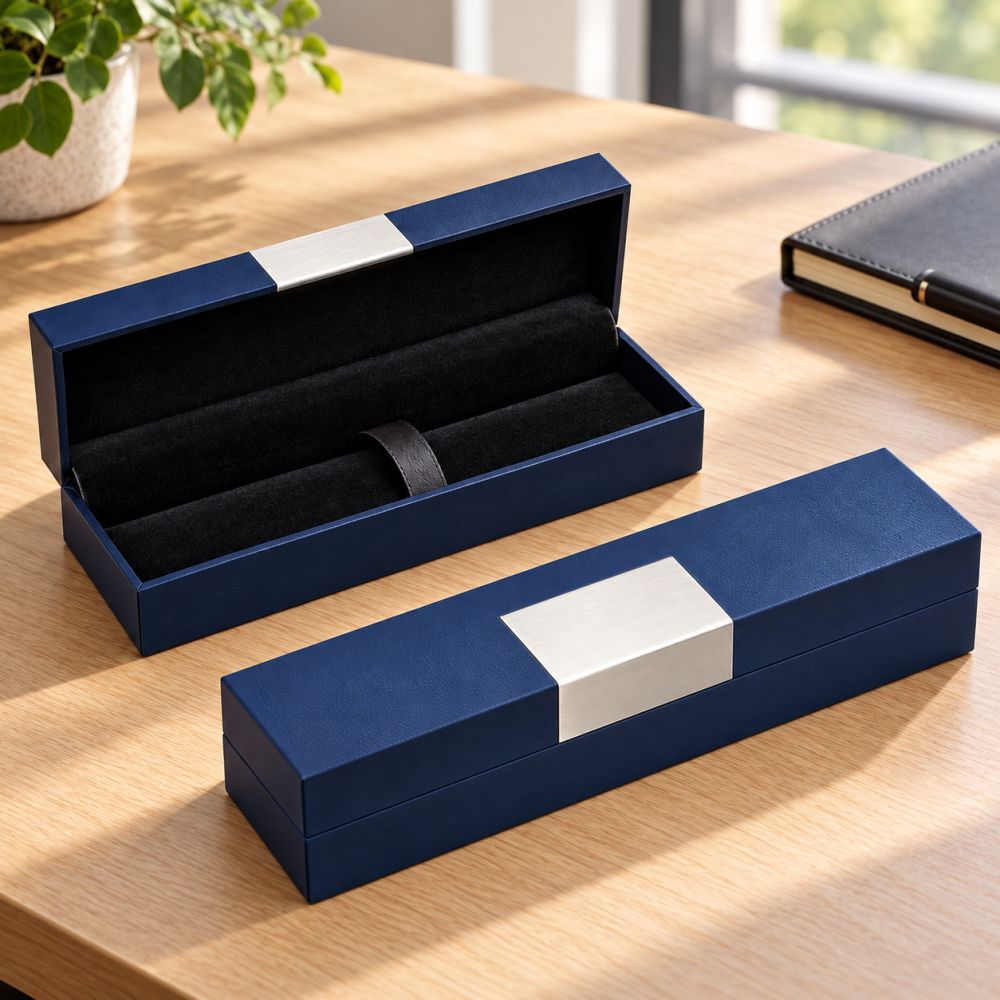 Black and blue SIGNATURE pen boxes on a desk, one open to show the black flannelette lining and strap, both with a silver aluminium plate on the lid