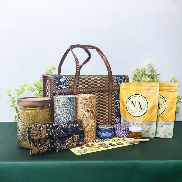 Rattan basket with a glass canister under a wooden lid, batik tissue box and pouches, candle tins and a yellow snack pouch.