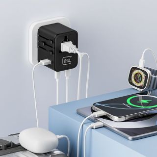 Black travel adapter plugged into a wall socket, charging a phone, a smartwatch and earbuds through white cables on a blue desk